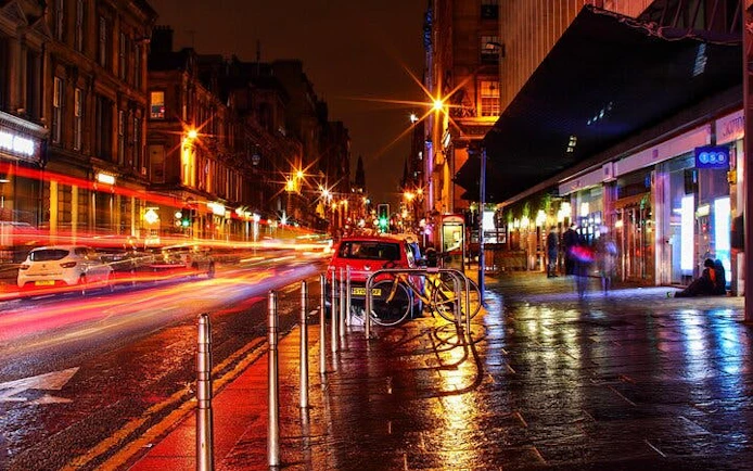 Nighttime street scene in Glasgow with blurred car lights, part of the Ghosts of Glasgow self-guided city exploration game.