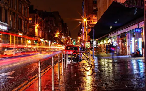 Nighttime street scene in Glasgow with blurred car lights, part of the Ghosts of Glasgow self-guided city exploration game.