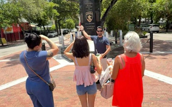 Tour guide leading a group in Little Havana, Miami, near a monument, highlighting Cuban culture.