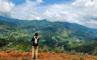 Traveler photographing Mu Cang Chai's terraced rice fields with mountains in the background.
