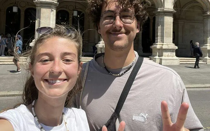 Two people smiling in front of a historic building in Vienna during a self-guided city exploration game.