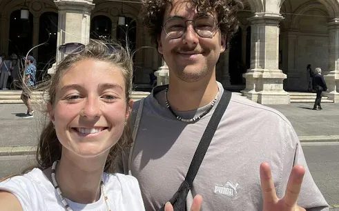 Two people smiling in front of a historic building in Vienna during a self-guided city exploration game.