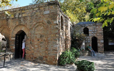 House of the Virgin Mary in Ephesus, stone building with visitors entering, surrounded by trees.