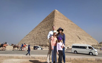 Family posing in front of the Pyramid of Giza during a guided tour with camel ride and ATV experience.