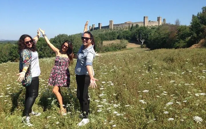 Tourists enjoying a sunny day in a field near the medieval walls of Monteriggioni, Tuscany.