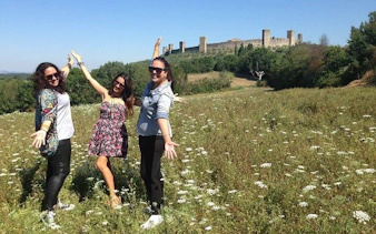 Tourists enjoying a sunny day in a field near the medieval walls of Monteriggioni, Tuscany.