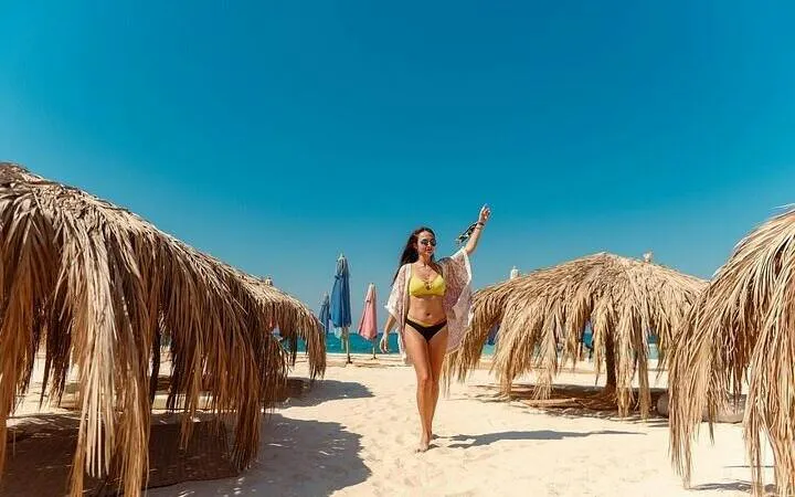 Private speedboat trip guest walking on sandy beach with straw umbrellas, Hula Hula Island, Hurghada.