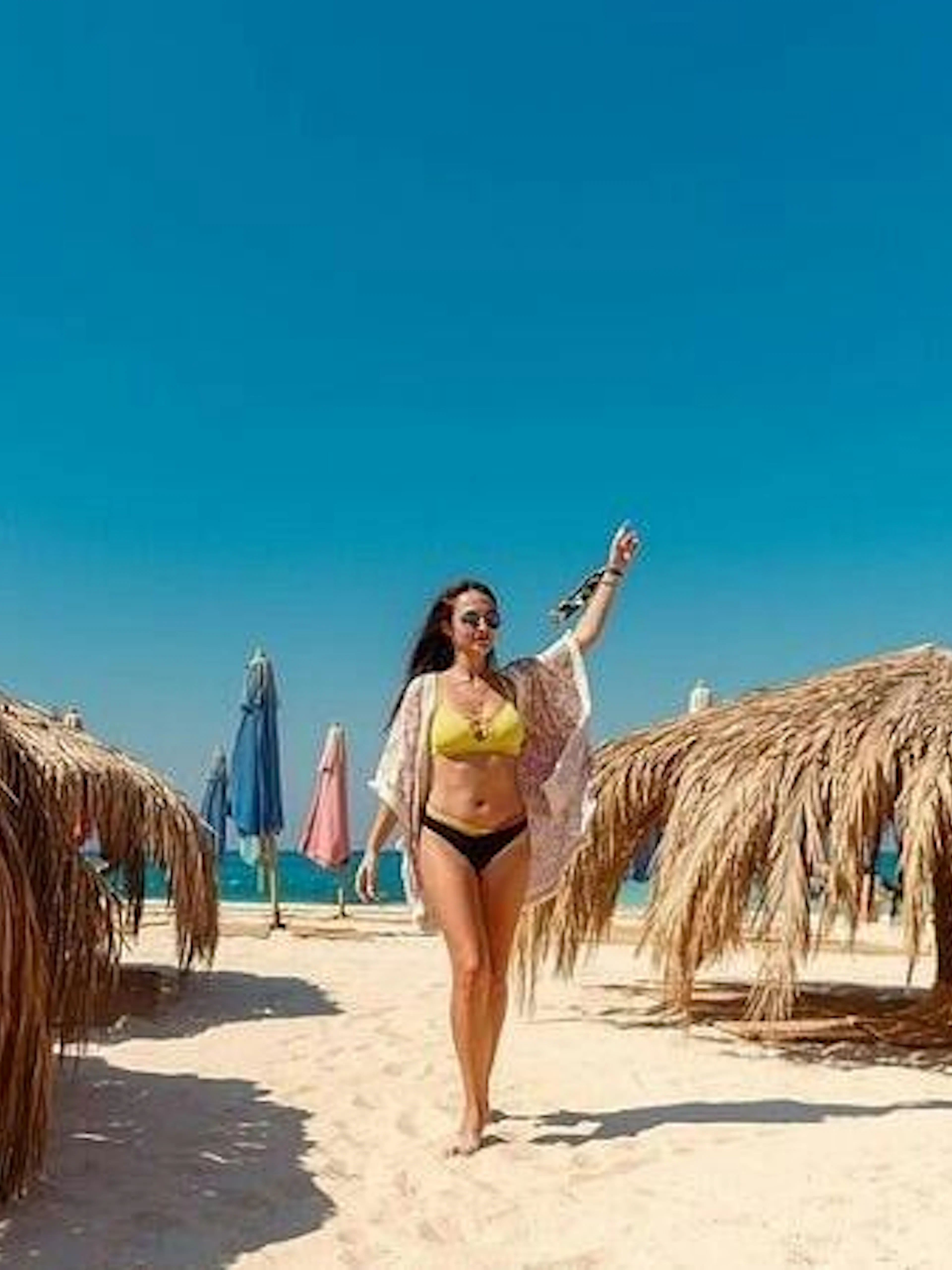 Private speedboat trip guest walking on sandy beach with straw umbrellas, Hula Hula Island, Hurghada.