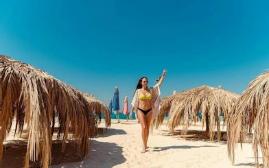 Private speedboat trip guest walking on sandy beach with straw umbrellas, Hula Hula Island, Hurghada.