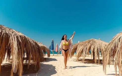 Private speedboat trip guest walking on sandy beach with straw umbrellas, Hula Hula Island, Hurghada.