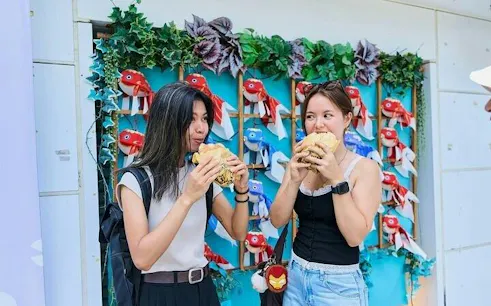 Two people enjoying street food in Asakusa, Tokyo, with colorful fish decorations in the background.