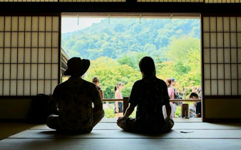 Visitors seated in a traditional Japanese room overlooking Arashiyama's lush landscape, Kyoto.