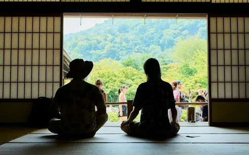 Visitors seated in a traditional Japanese room overlooking Arashiyama's lush landscape, Kyoto.