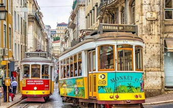 Lisbon trams on a narrow street, part of a self-guided walking tour using a mobile app.