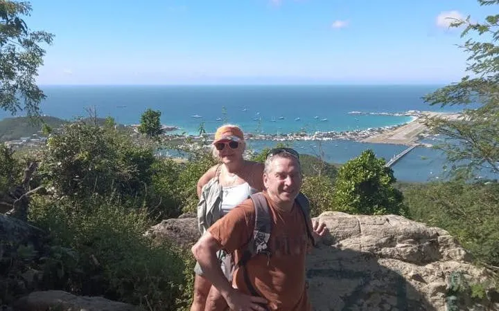 Hikers enjoying panoramic view from St. Maarten's highest point with ocean and marina in background.