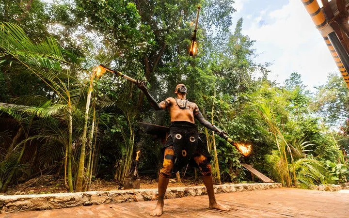 Performer juggling fire during cultural show in lush setting, part of snorkeling tour with cenotes and tequila tasting.