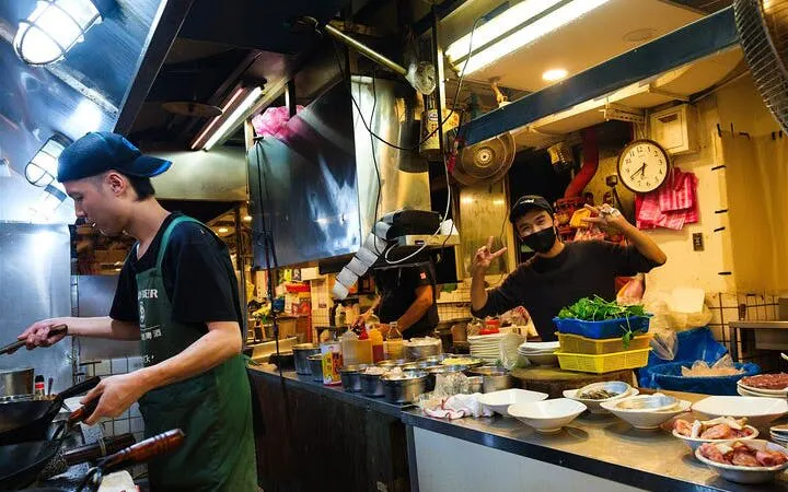 Chef cooking in a Taipei street food stall with various ingredients on the counter.