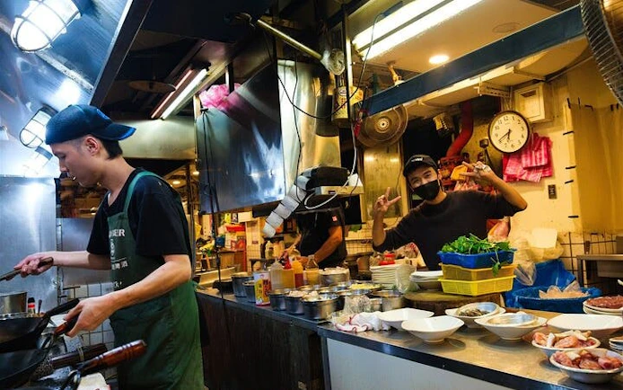 Chef cooking in a Taipei street food stall with various ingredients on the counter.