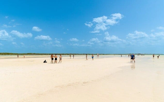 Visitors walking on the sandy beach of Punta Mosquito, Holbox Island under a clear blue sky.