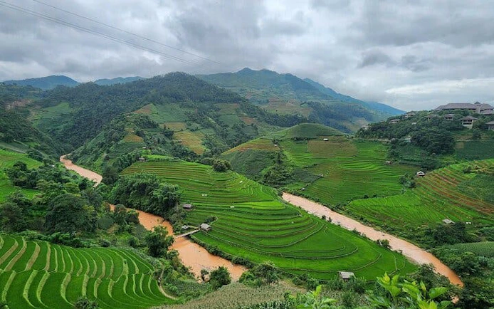Terraced rice fields and river in Mu Cang Chai, Vietnam, with mountains in the background.