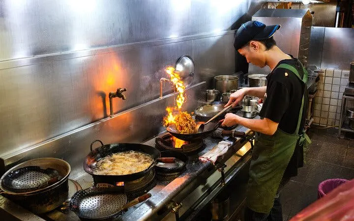 Chef cooking with flames in a Taipei kitchen during a local food tour.