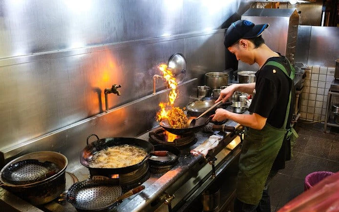 Chef cooking with flames in a Taipei kitchen during a local food tour.