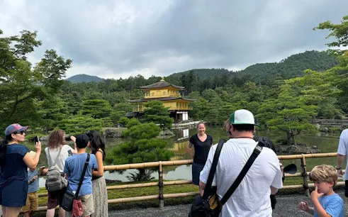 Visitors at Kinkakuji, the Golden Pavilion, Kyoto, with lush greenery and reflective pond.