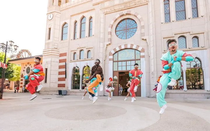 Performers in colorful costumes jumping in front of The Land of Legends Theme Park entrance.