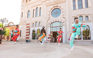 Performers in colorful costumes jumping in front of The Land of Legends Theme Park entrance.
