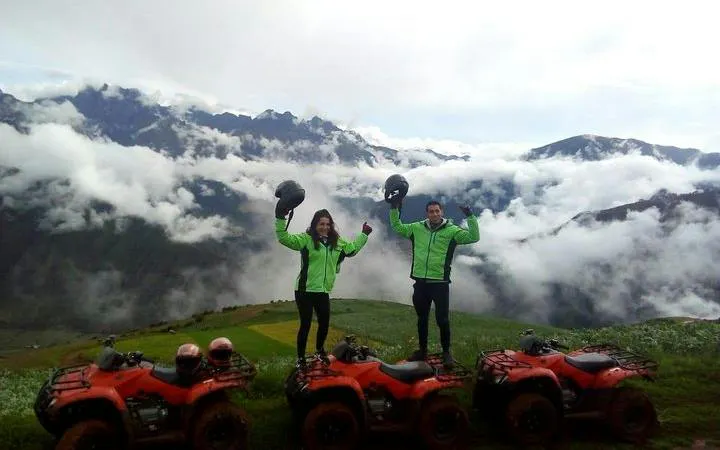 ATV riders with helmets in Maras, overlooking Andes mountains and clouds, Cusco tour.