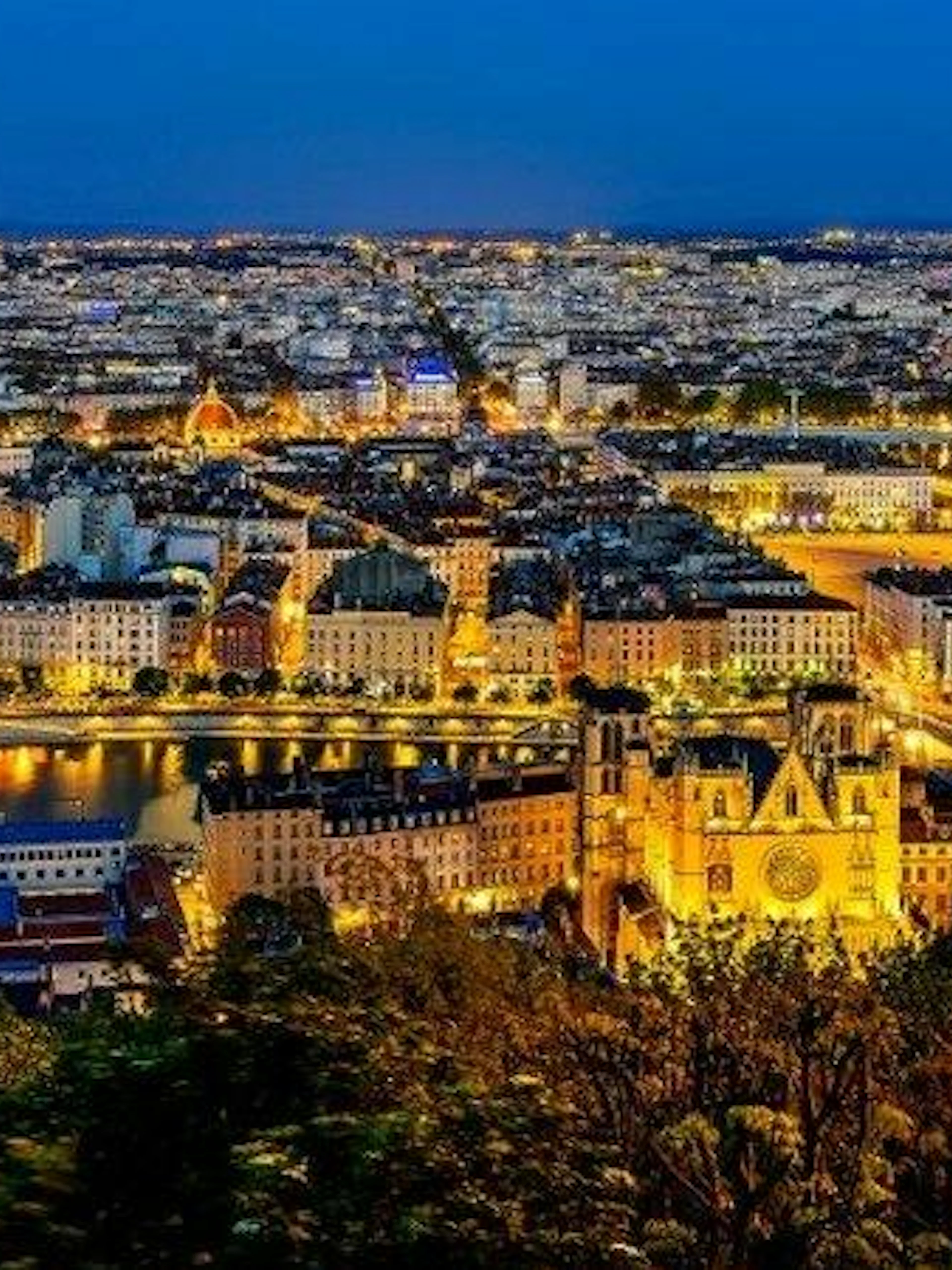 Lyon cityscape at night with illuminated buildings and the Saône River, viewed from a high vantage point.