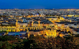 Lyon cityscape at night with illuminated buildings and the Saône River, viewed from a high vantage point.