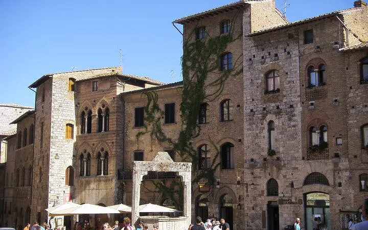 Historic stone buildings in Siena, Italy, with ivy-covered walls and a bustling street scene.