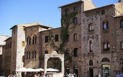 Historic stone buildings in Siena, Italy, with ivy-covered walls and a bustling street scene.