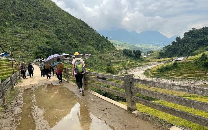 Tourists walking along a muddy path in Sapa with terraced rice fields and mountains in the background.