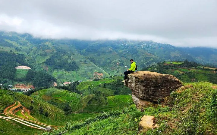 Person sitting on a rock overlooking terraced rice fields in Sapa, Vietnam.