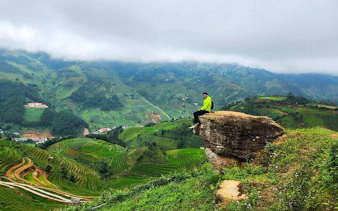 Person sitting on a rock overlooking terraced rice fields in Sapa, Vietnam.