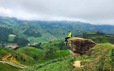 Person sitting on a rock overlooking terraced rice fields in Sapa, Vietnam.