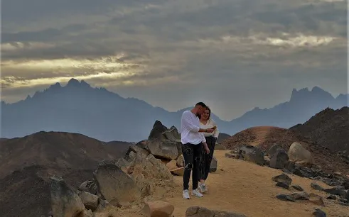 Couple standing on rocky desert path with mountains at sunrise, Sharm El Sheikh.
