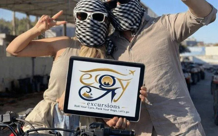 Couple holding a sign for a Cairo guided desert quad bike tour at Giza Pyramids.