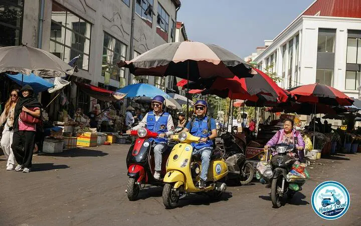 Vespa riders exploring a bustling market street in Hanoi during a half-day tour.