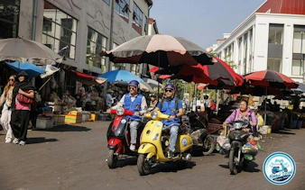 Vespa riders exploring a bustling market street in Hanoi during a half-day tour.