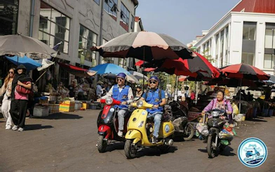 Vespa riders exploring a bustling market street in Hanoi during a half-day tour.
