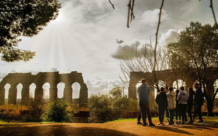 Group of people on a guided tour near ancient Roman aqueducts on the Appian Way, Rome.