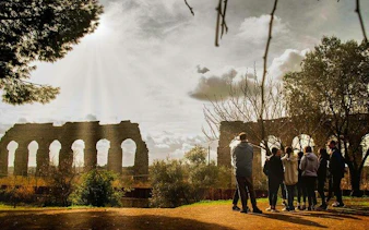 Group of people on a guided tour near ancient Roman aqueducts on the Appian Way, Rome.
