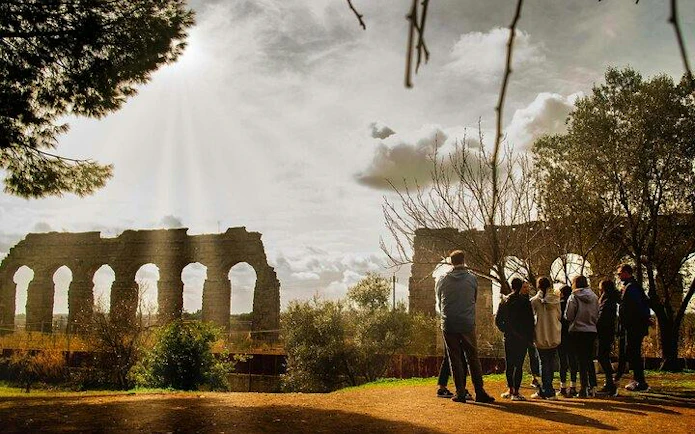 Group of people on a guided tour near ancient Roman aqueducts on the Appian Way, Rome.