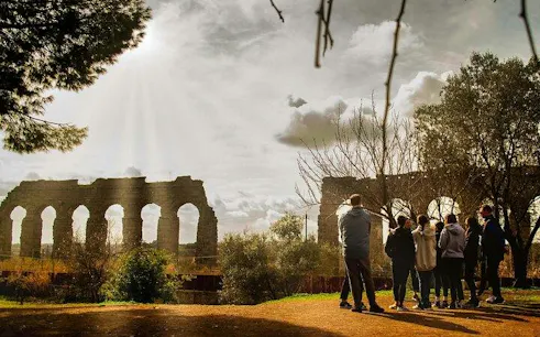 Group of people on a guided tour near ancient Roman aqueducts on the Appian Way, Rome.