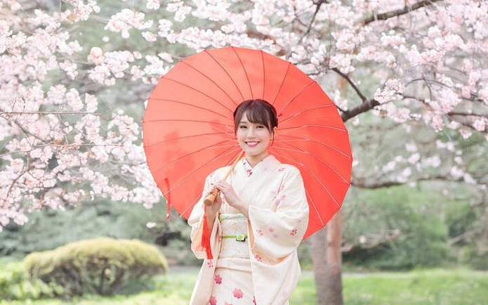 Kimono rental experience in Shinjuku Gyoen, Tokyo, with cherry blossoms and red umbrella.