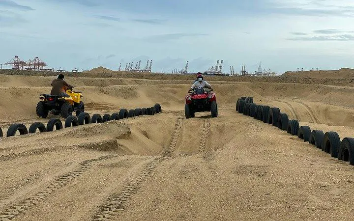 ATV riders navigating sandy terrain near New York port cranes.