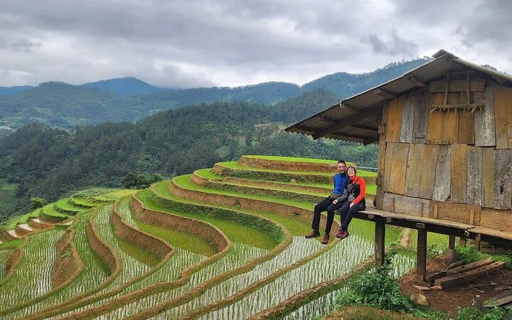 Terraced rice fields in Mu Cang Chai with travelers sitting by a wooden hut.